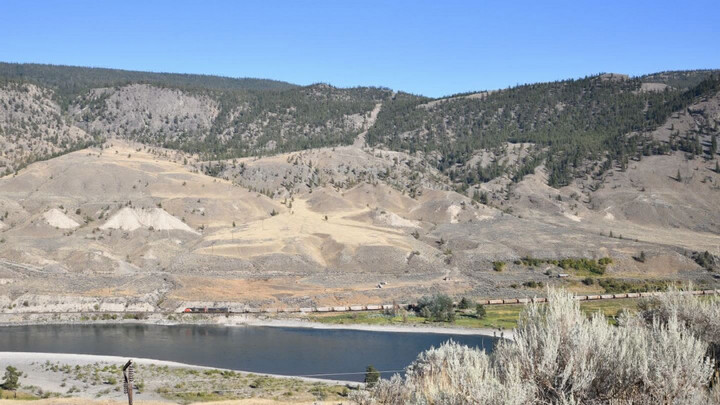 A river flowing alongside a trainline in a dry valley.