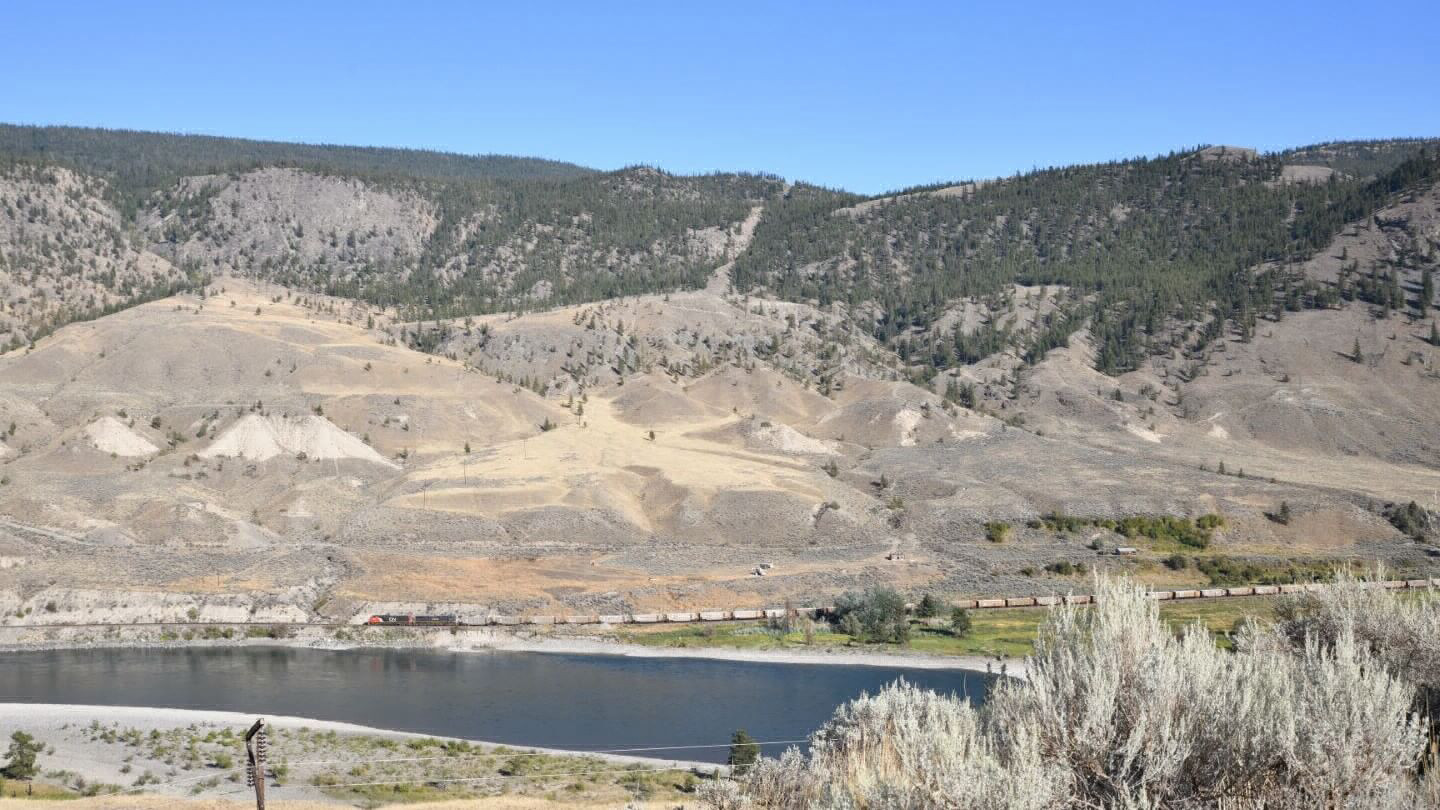 A river flowing alongside a trainline in a dry valley.
